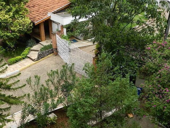 Un barrio residencial con una casa de techo a tejas, entrada protegida por una reja y abundante vegetación alrededor de la propiedad.