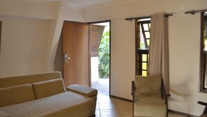A room with a sofa, a chair, a wooden door, and a window with curtains. - Chalé Hotel (Bauru)