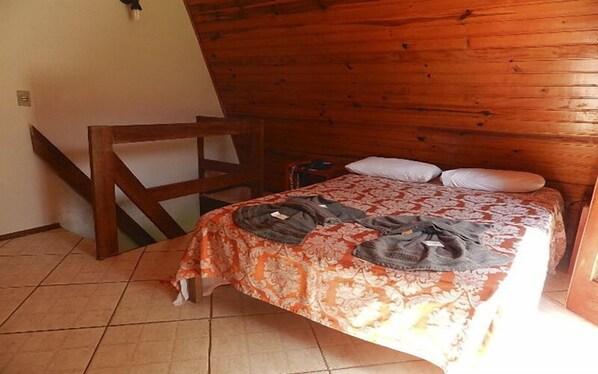 Un dormitorio con cabecera de madera, cama con colcha estampada y una silla.