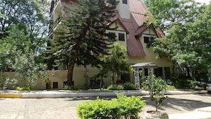 A building with a sloped roof, multiple windows, and a surrounding garden with various plants and a small pond. - Chalé Hotel (Bauru)