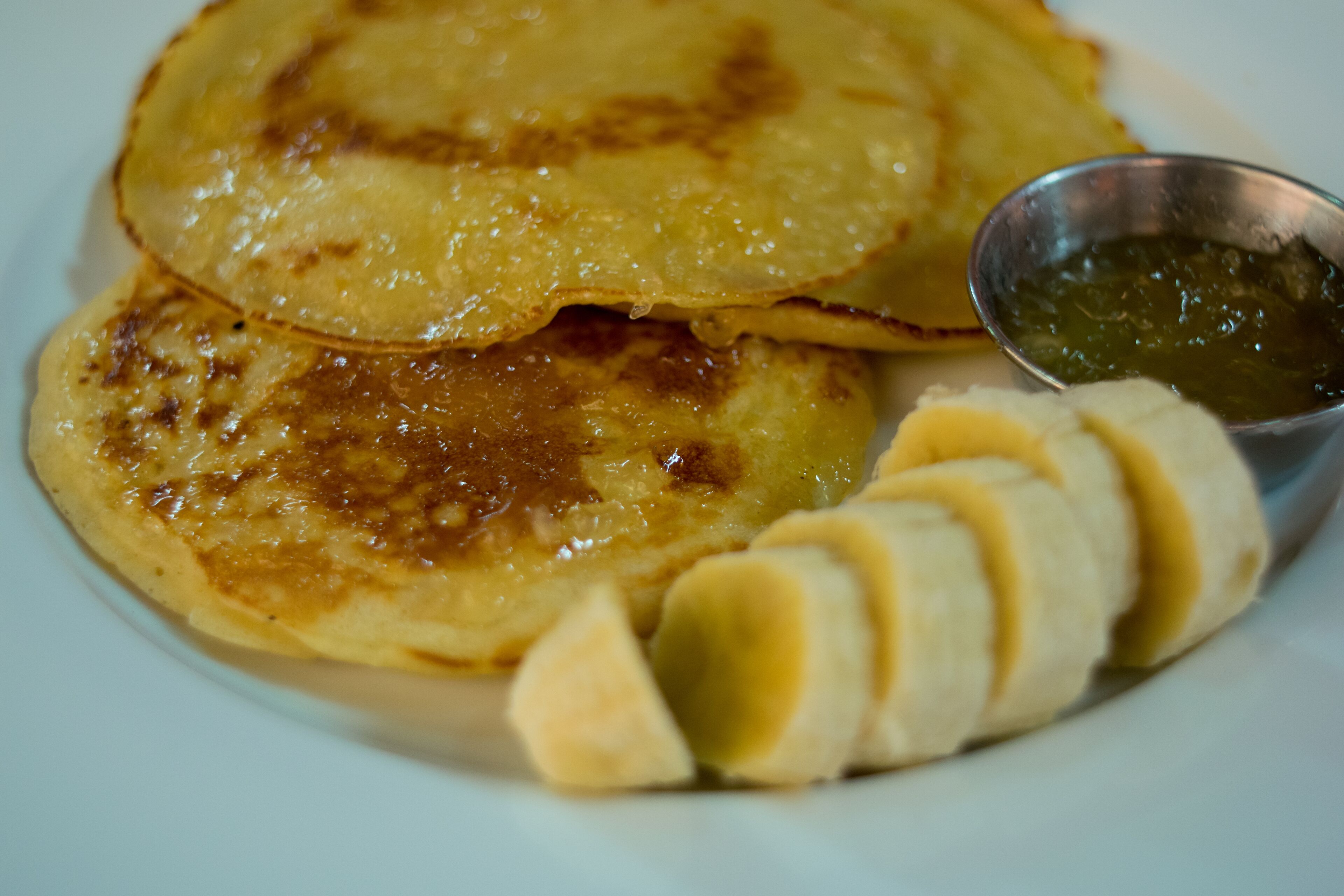 Un plato de panqueques, un cuenco pequeño de jarabe y rodajas de plátano.