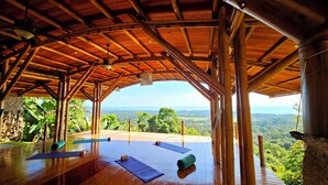 Une salle de yoga en plein air avec des poutres en bois, une vue sur le paysage et des tapis de yoga.