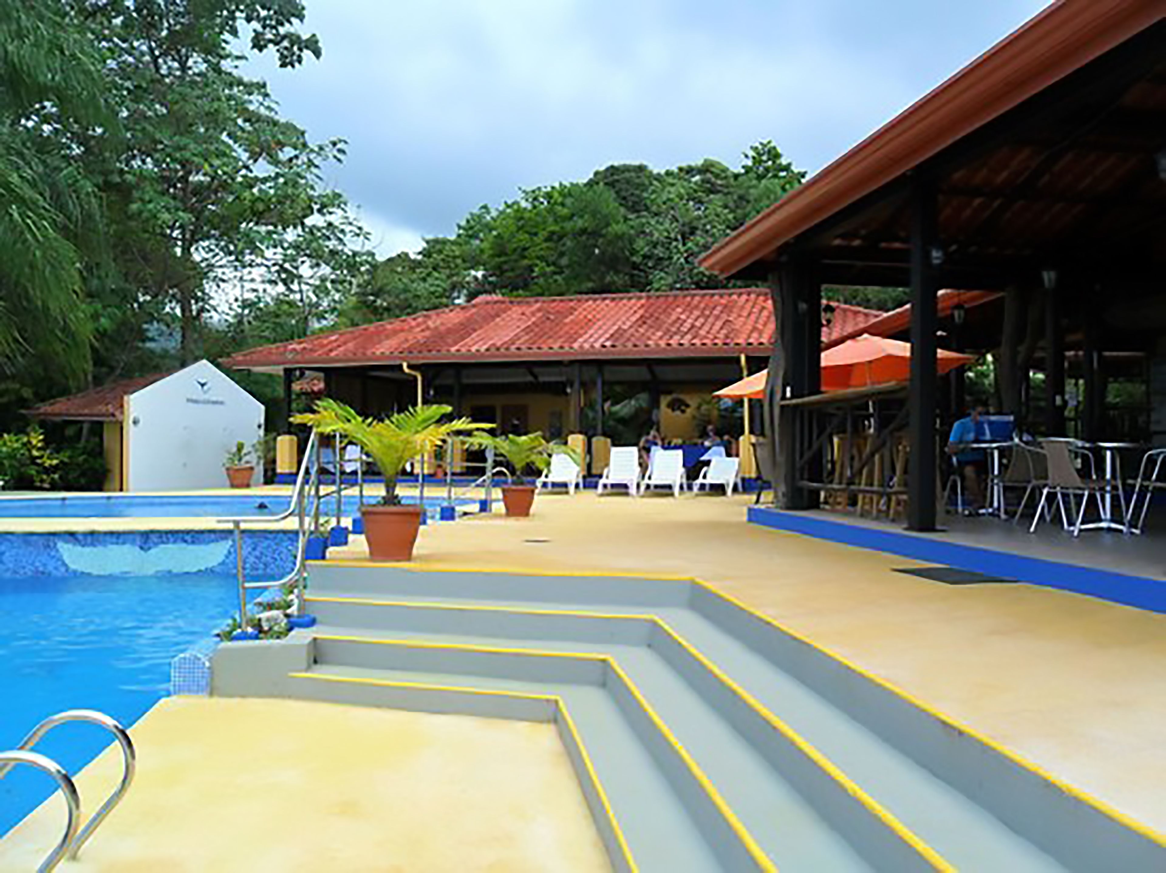 Área da piscina com degraus que levam à água, cercada por espreguiçadeiras e um espaço coberto para relaxar.
