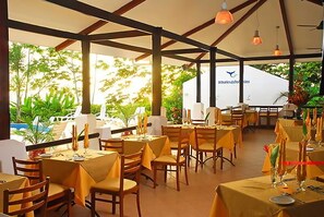 An outdoor dining area with tables set for two, featuring yellow tablecloths and wooden chairs. - Vista Ballena (Bahía Ballena)