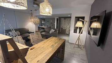 A modern living room with a wooden dining table, grey sofas, and hanging wicker lamps.