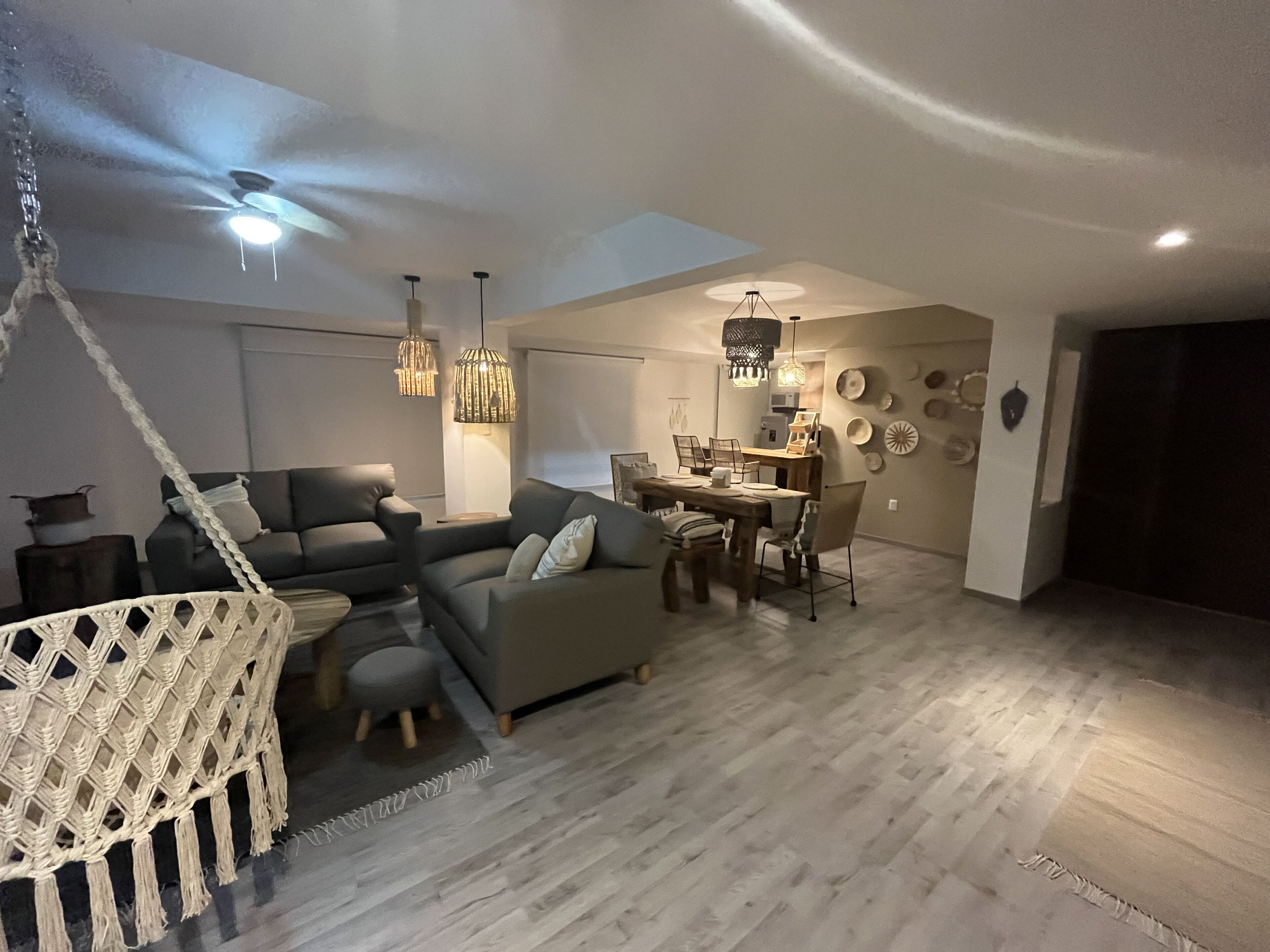 Een moderne woonkamer met een bank, eettafel en stoelen. Er is een hangstoel en een plafondventilator.