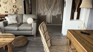 A modern living room with a grey sofa, wicker chairs, a wooden coffee table, and a macrame wall hanging.
