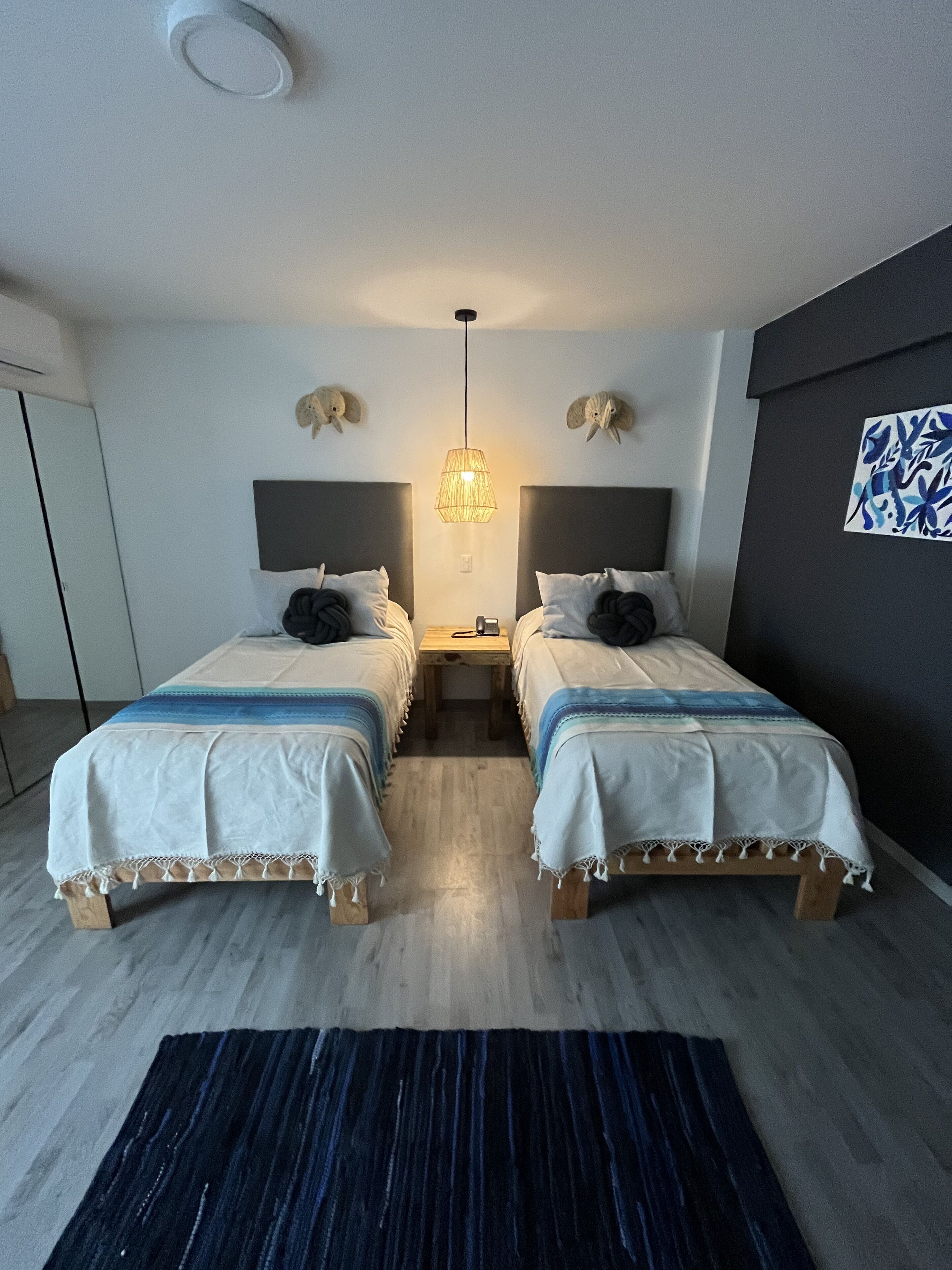 Ein Doppelzimmer mit zwei Betten, einem Nachttisch, einer Hängeleuchte und einem Wandbild.