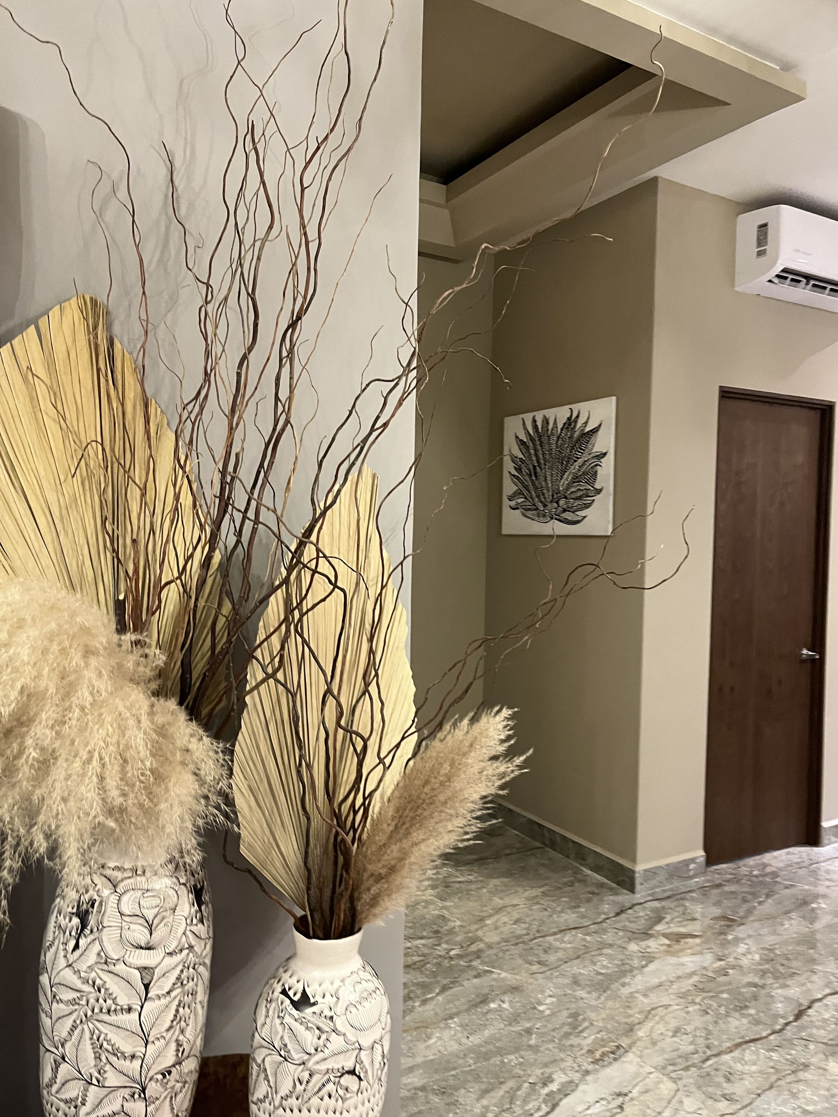 Un corridoio con due vasi di pannocchie di grano, un'opera d'arte a parete e una porta.