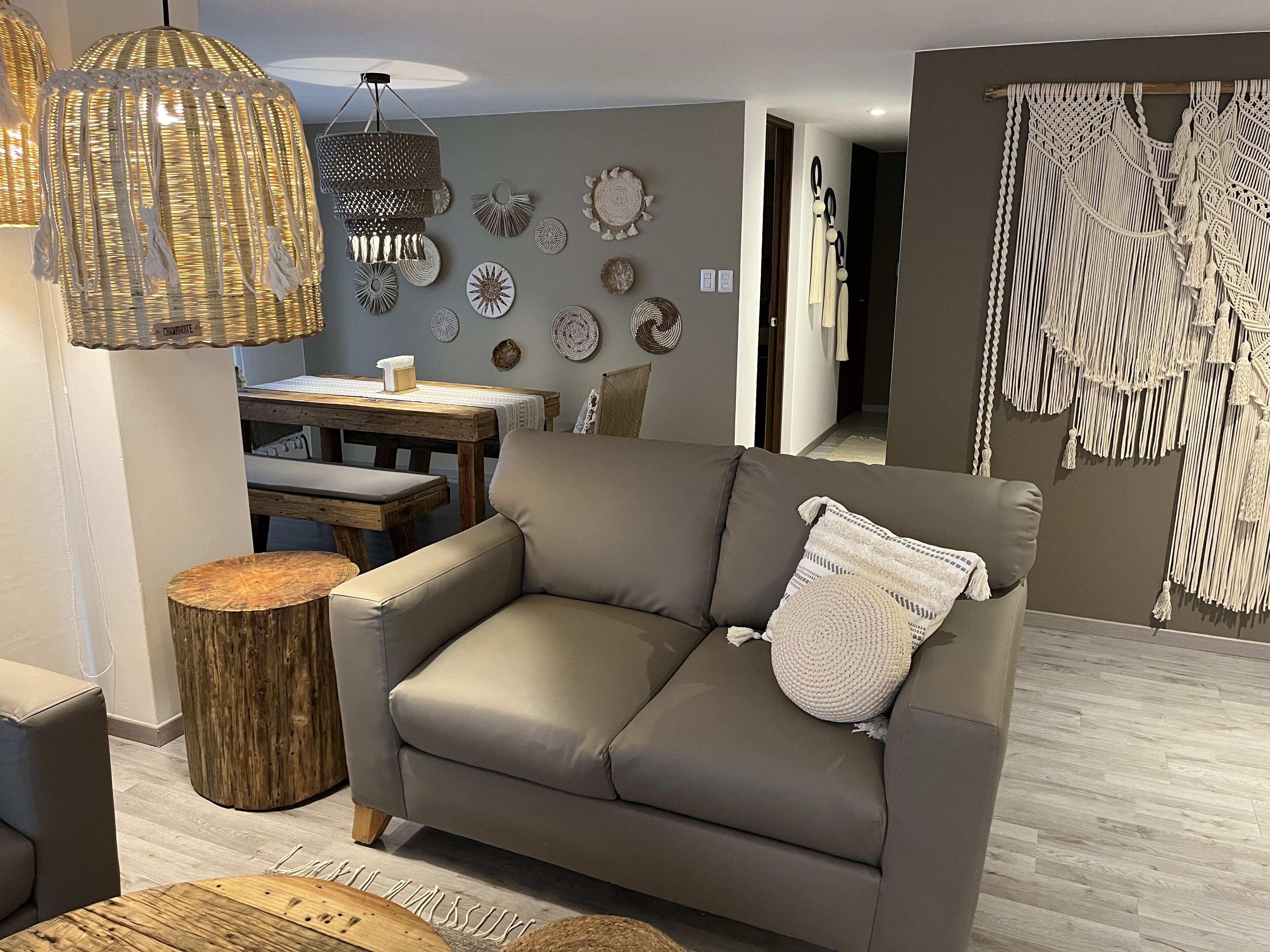 A modern living room with a grey sofa, wooden side table, and a dining area with a wooden table and chairs.