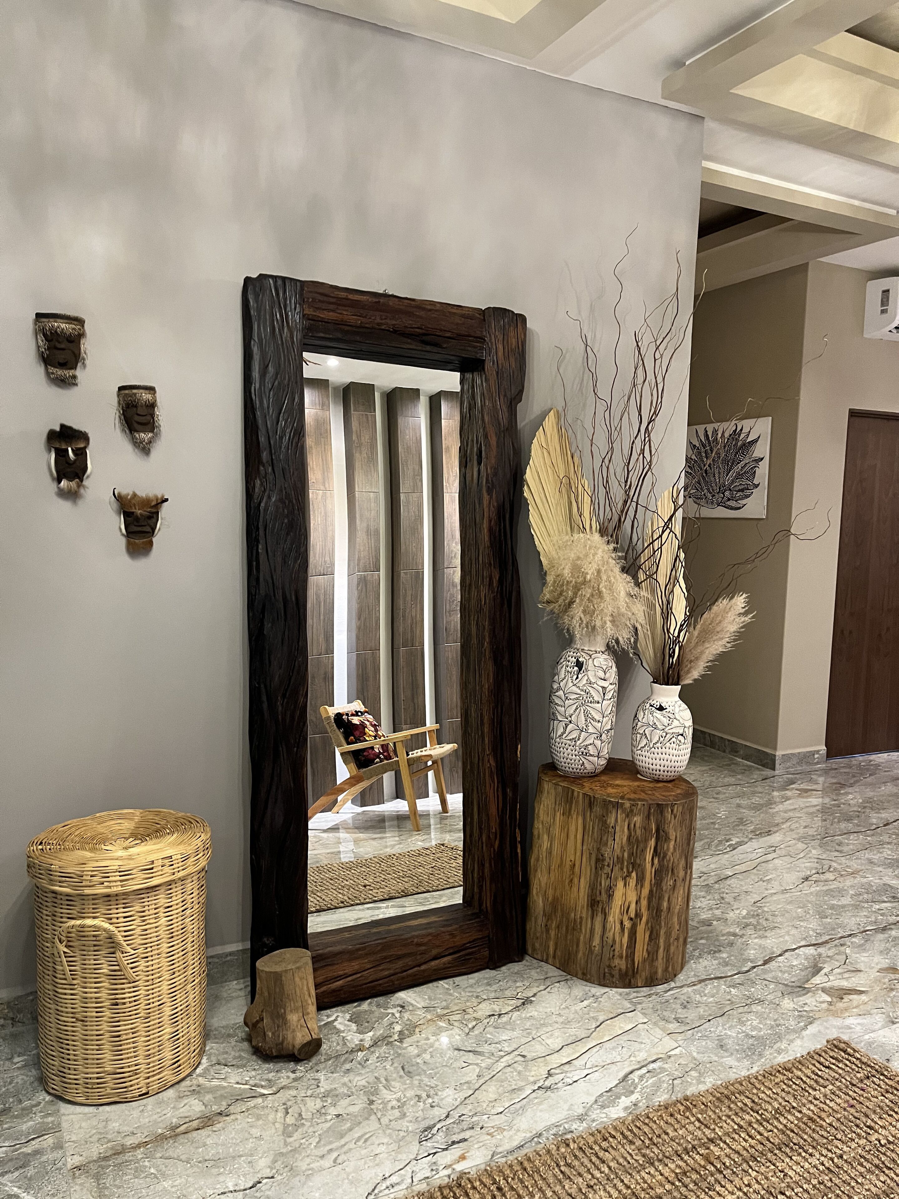 A modern interior with a large mirror, decorative wall pieces, a wicker basket, and a wooden stool with vases.