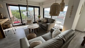 A modern living room with a sofa, chairs, a coffee table, and a balcony with a view. - Zen Suites by Regente (Oaxaca)
