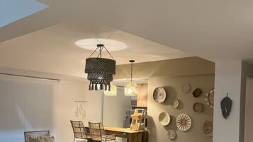 A dining area with a wooden table and chairs, a hanging light fixture, and decorative plates on the wall.