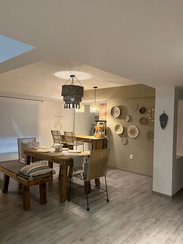 A dining area with a wooden table and chairs, a hanging light fixture, and decorative plates on the wall. - Zen Suites by Regente (Oaxaca)