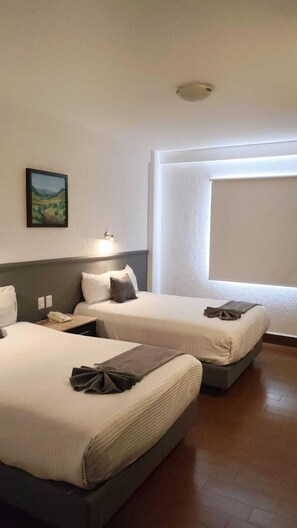 Habitació d'hotel amb dos llits, un quadre a la paret i una finestra que deixa entrar llum natural.