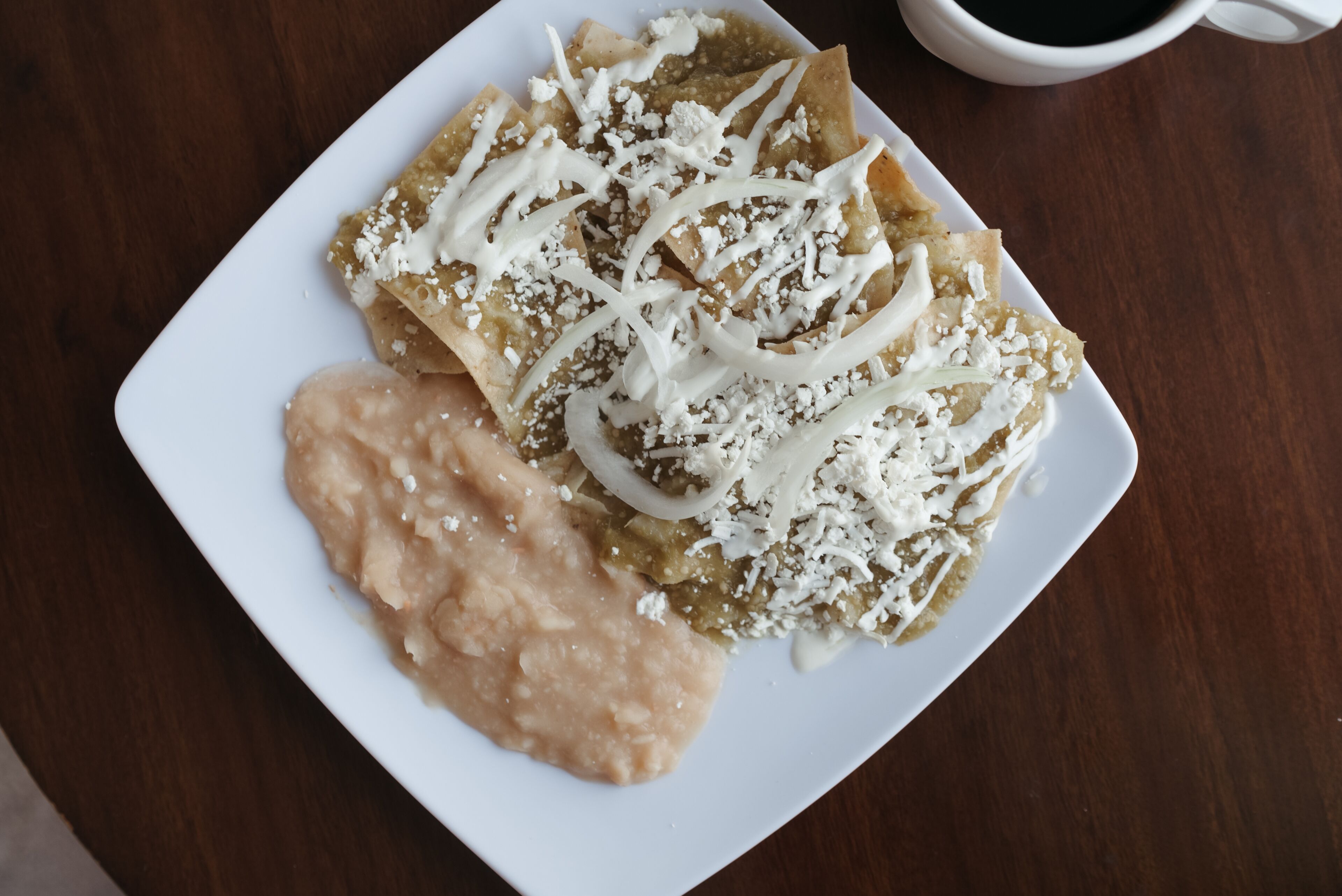 A plate of crepes with white sauce and shredded cheese, accompanied by a cup of coffee on a wooden table.