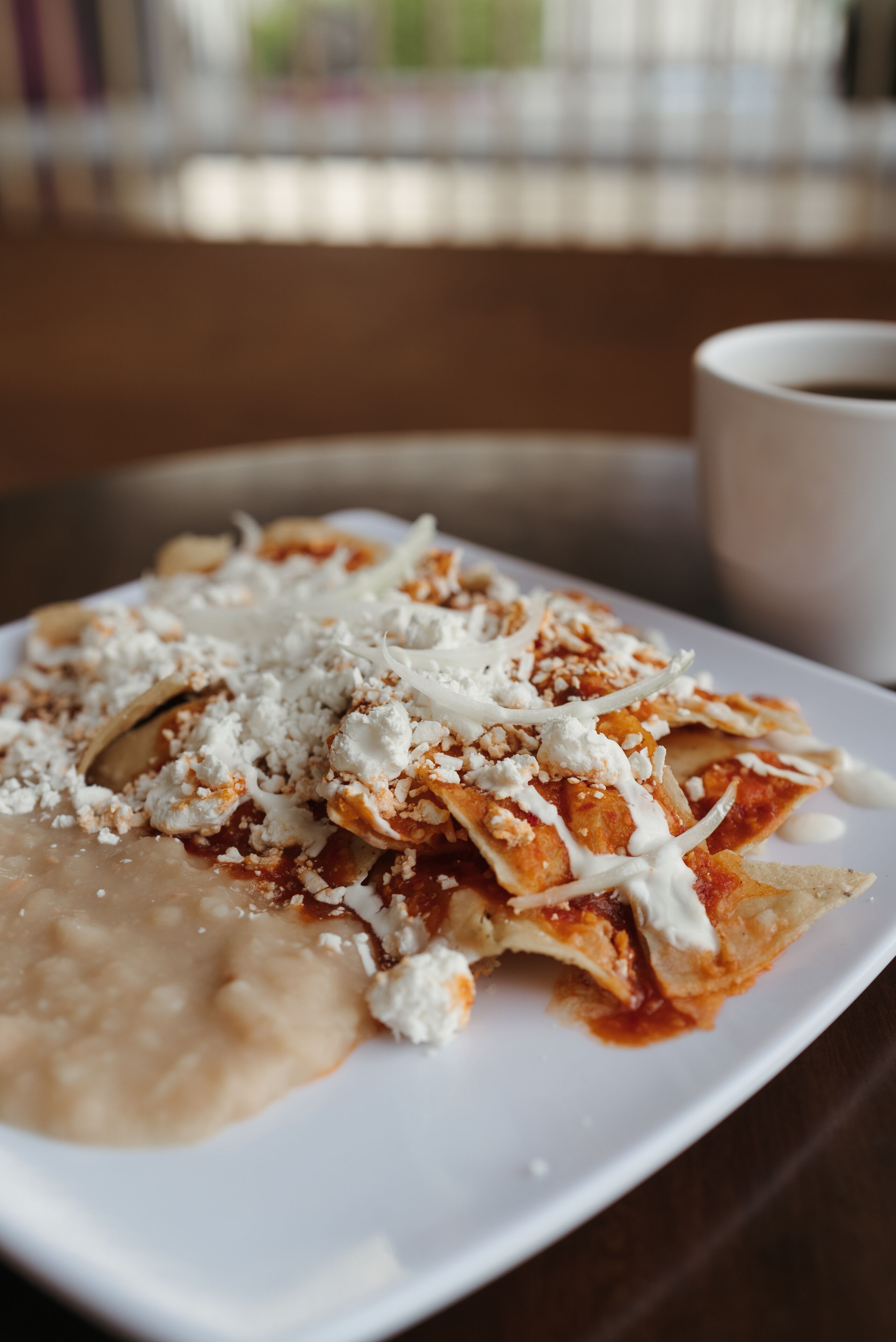 A plate of enchiladas with cheese and sauce, accompanied by a cup of coffee on a table.