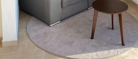 Ein Wohnzimmer mit grauem Sofa, zwei gerahmten abstrakten Gemälden, einem runden Holztisch und einem grauen Teppich.