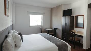 Una habitación de hotel con una cama grande, un escritorio, una silla, un televisor y una ventana.