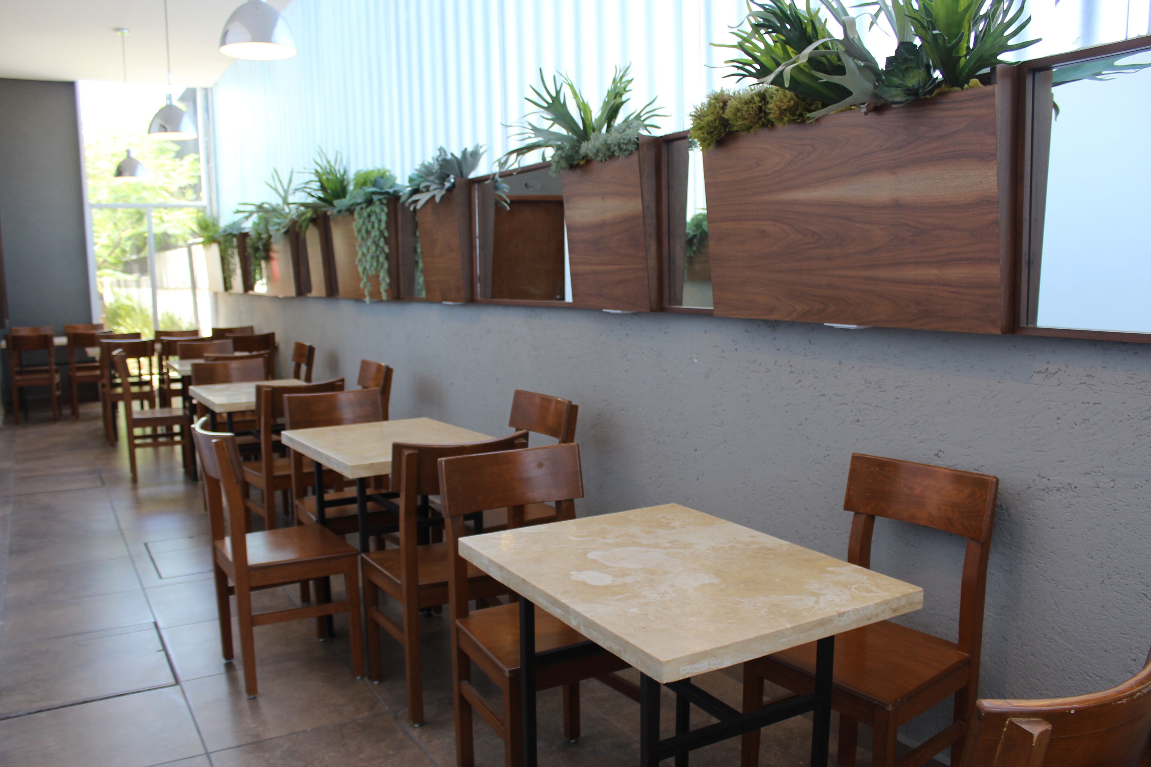 Interior de un restaurante con mesas y sillas de madera, suelo de baldosas y una pared decorada con jardineras verticales.