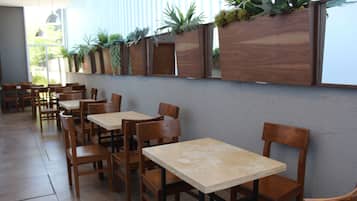Interior de un restaurante con mesas y sillas de madera, suelo de baldosas y una pared decorada con jardineras verticales.
