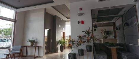 A modern lobby with a reception desk, seating area, potted plants, and a staircase.