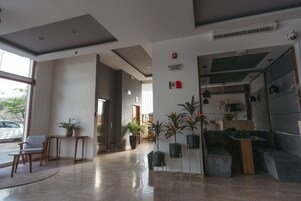 Un vestíbulo moderno con mostrador de recepción, zona de estar, plantas en macetas y una escalera.