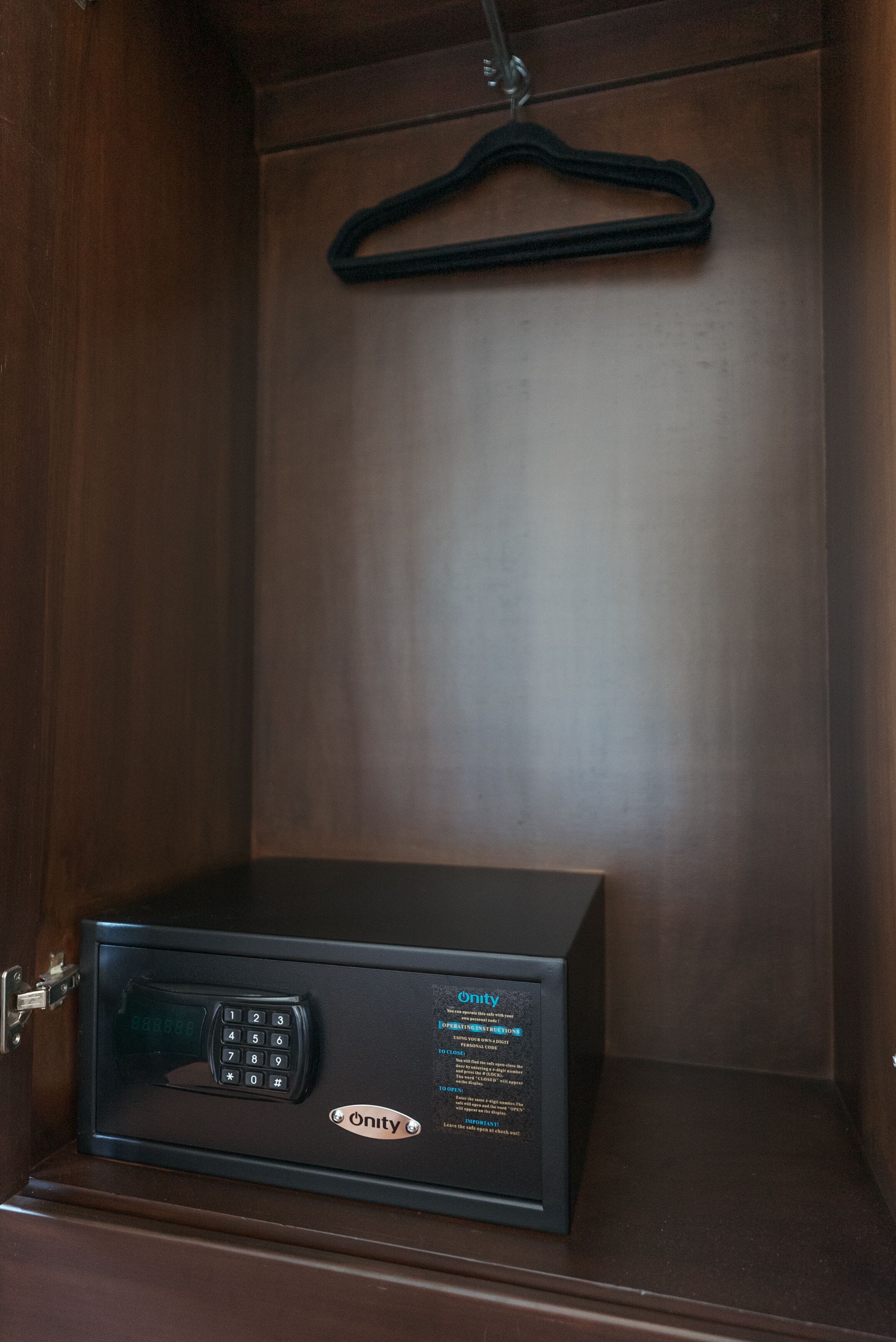 A safe with a keypad and a hanging hanger in a wooden cabinet.