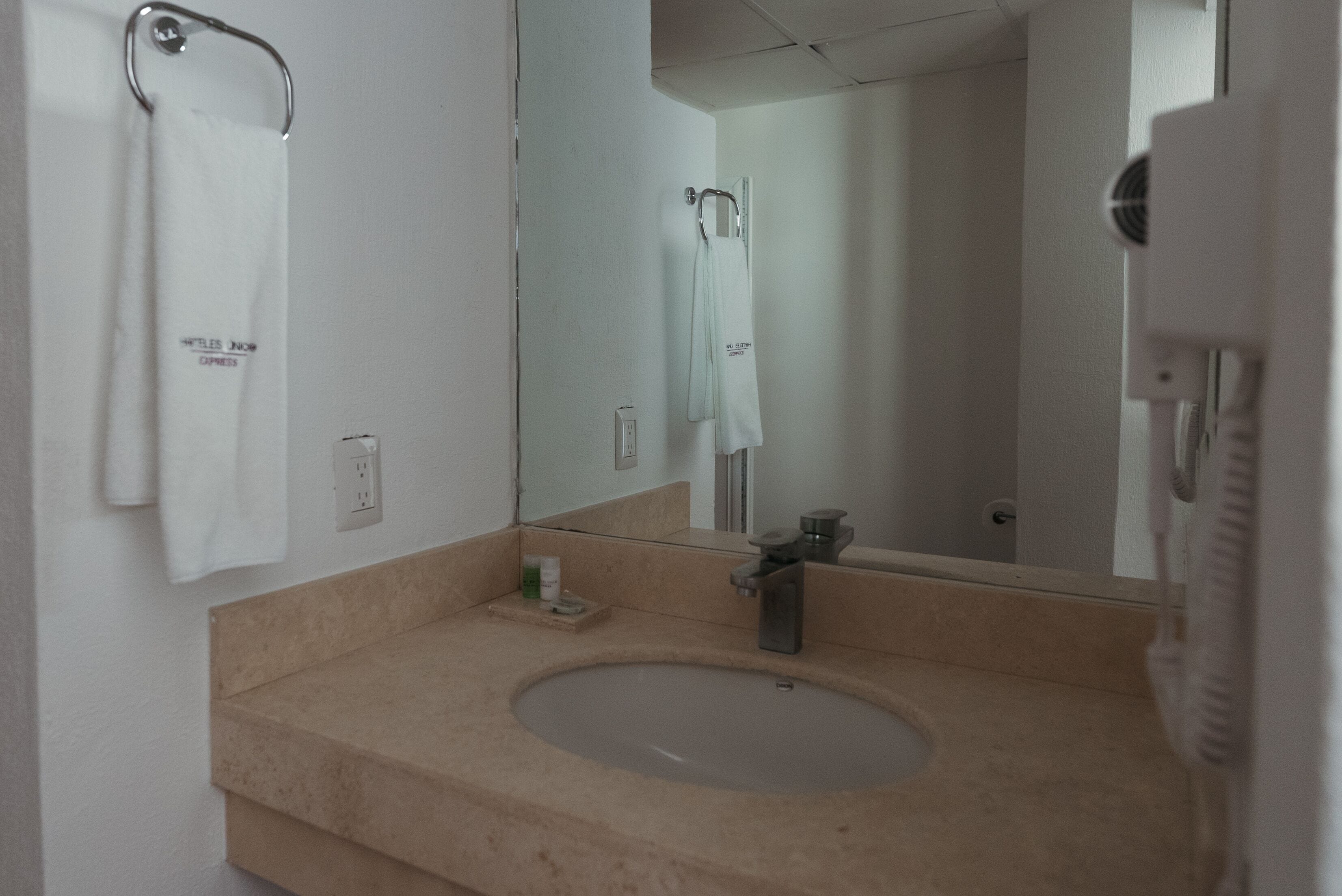 Un baño con un lavabo beige, un espejo y dos toallas blancas colgadas en ganchos.