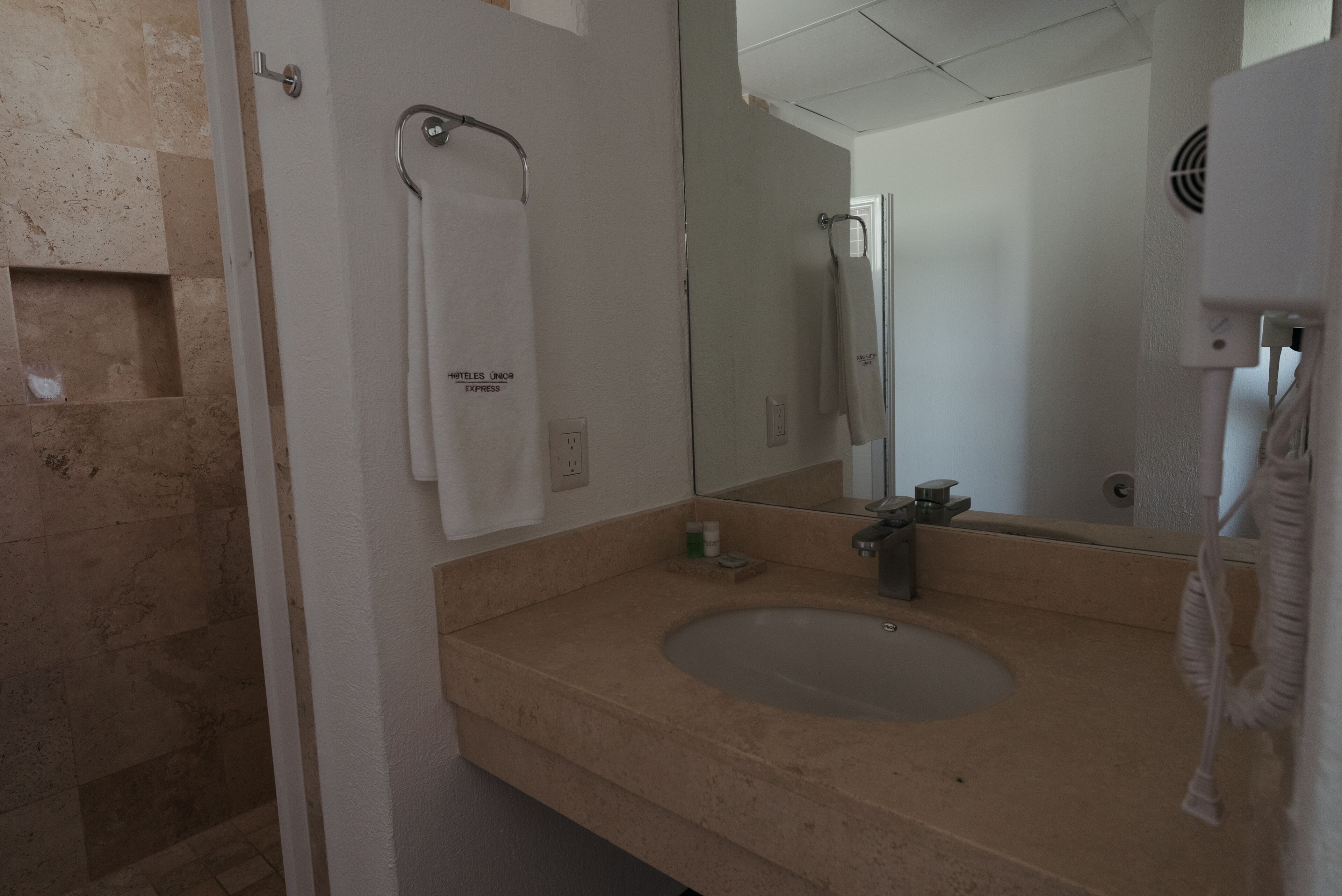 A bathroom with a beige sink, a towel hanging on a rack, a mirror, and a handheld showerhead.