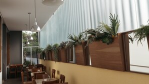 A restaurant with wooden tables and chairs, hanging pendant lights, and a row of potted plants along the wall. - Hoteles Unico Express (León)