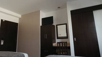 A hotel room with a bed, a desk with a chair, a wardrobe, and a television on top of the wardrobe.
