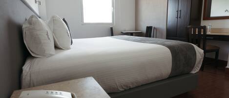 Habitación de hotel con cama, mesita de noche con teléfono, una pequeña mesa con sillas, ventana, escritorio con espejo y armario.