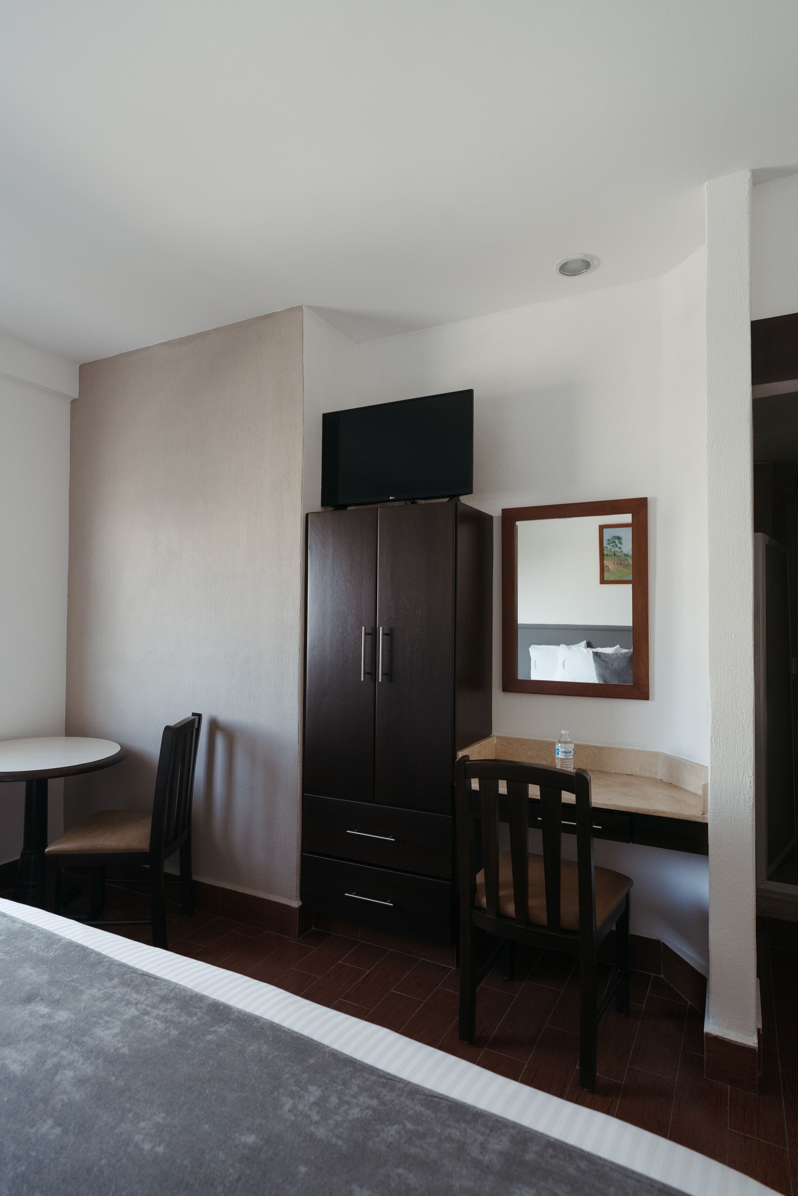 A compact hotel room with a single bed, a small desk with a chair, a television mounted above the desk, and a wardrobe.