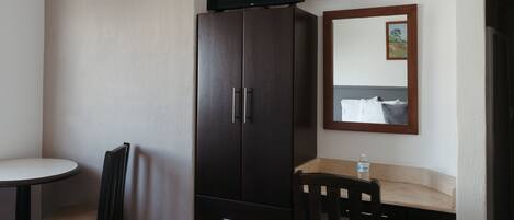 Una habitación de hotel pequeña con una cama individual, un escritorio y una silla, un televisor colocado sobre el escritorio y un armario.