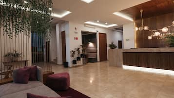 A modern hotel lobby with a reception desk, seating area, and a staircase leading to other floors.