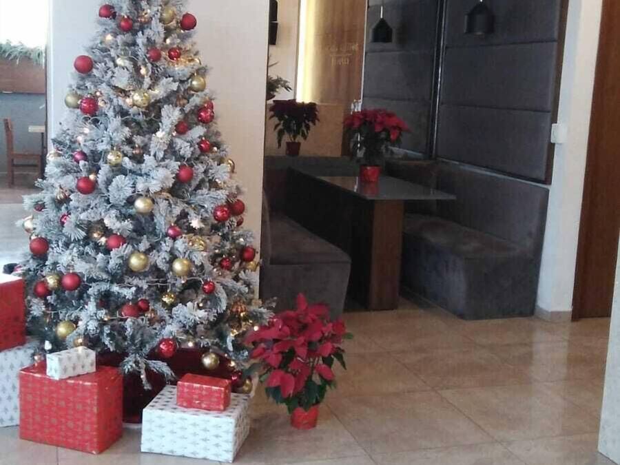 Un sapin de Noël décoré d’ornements et entouré de cadeaux, un panneau de sécurité et une plante en pot.