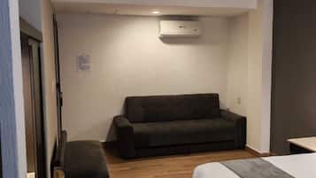 Una habitación con una cama, un sofá, un banco y un equipo de aire acondicionado en la pared.