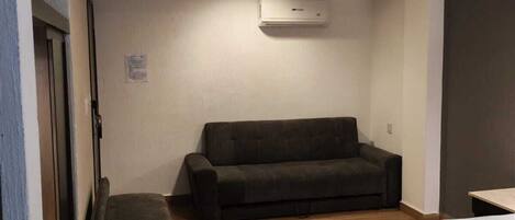 Een kamer met een bed, een bank, een houten bankje en een airconditioner aan de muur.