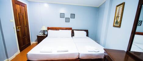 Una cama doble con ropa de cama blanca, una mesita de noche de madera con una lámpara y un cuadro en la pared.