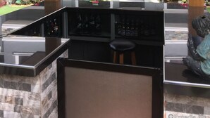 A bar area with a counter and stools, a ceiling fan, and a view of a building with windows decorated with red and white banners. - The Gabriella B&B (Tagbilaran)