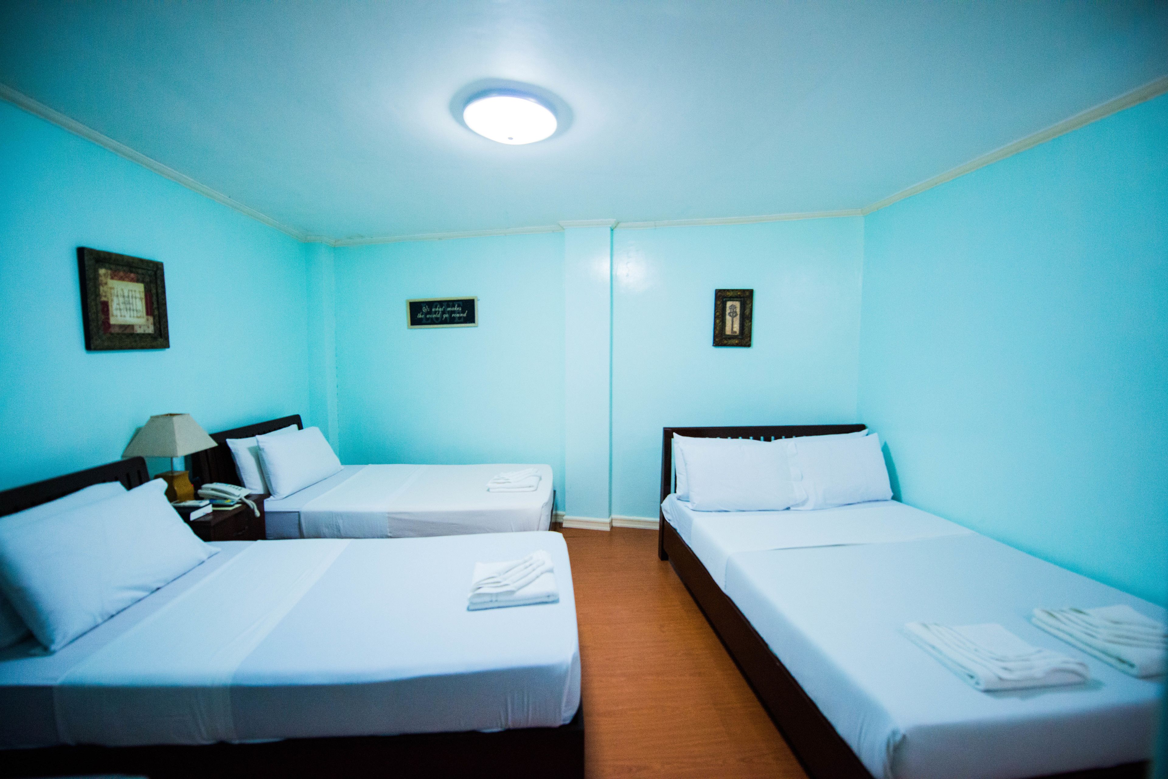 A hotel room with two single beds, a nightstand with a lamp, and a small table with a telephone.