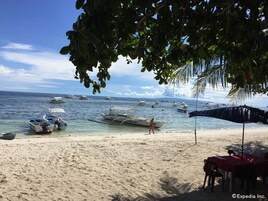 Una playa con barcos, una mesa con sillas y una persona caminando.