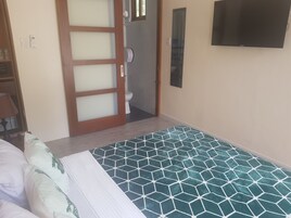 Una habitación de hotel con cama, baño con inodoro, ducha y televisor montado en la pared.