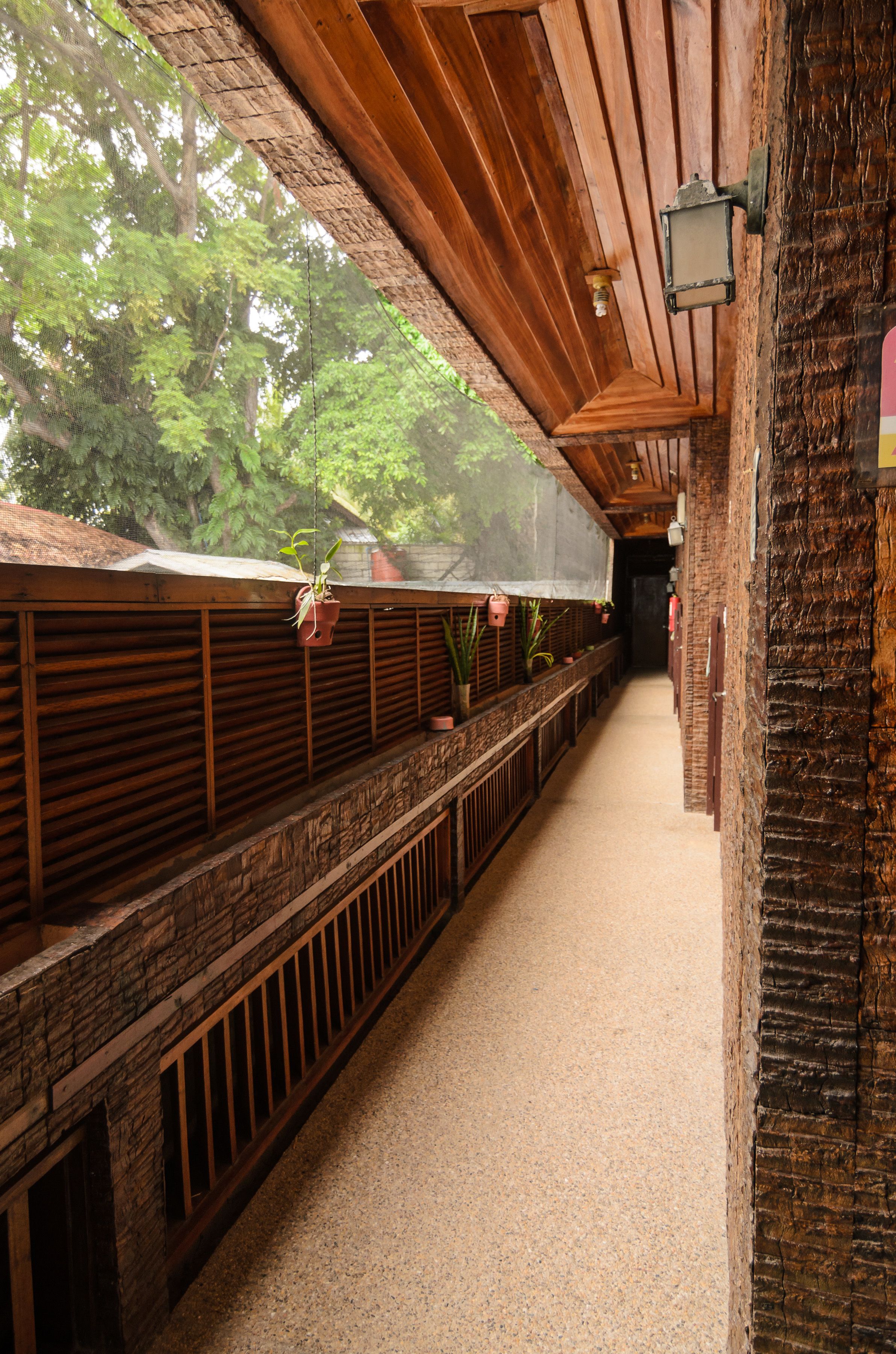 A corridor with wooden railings, potted plants, and a brick wall.