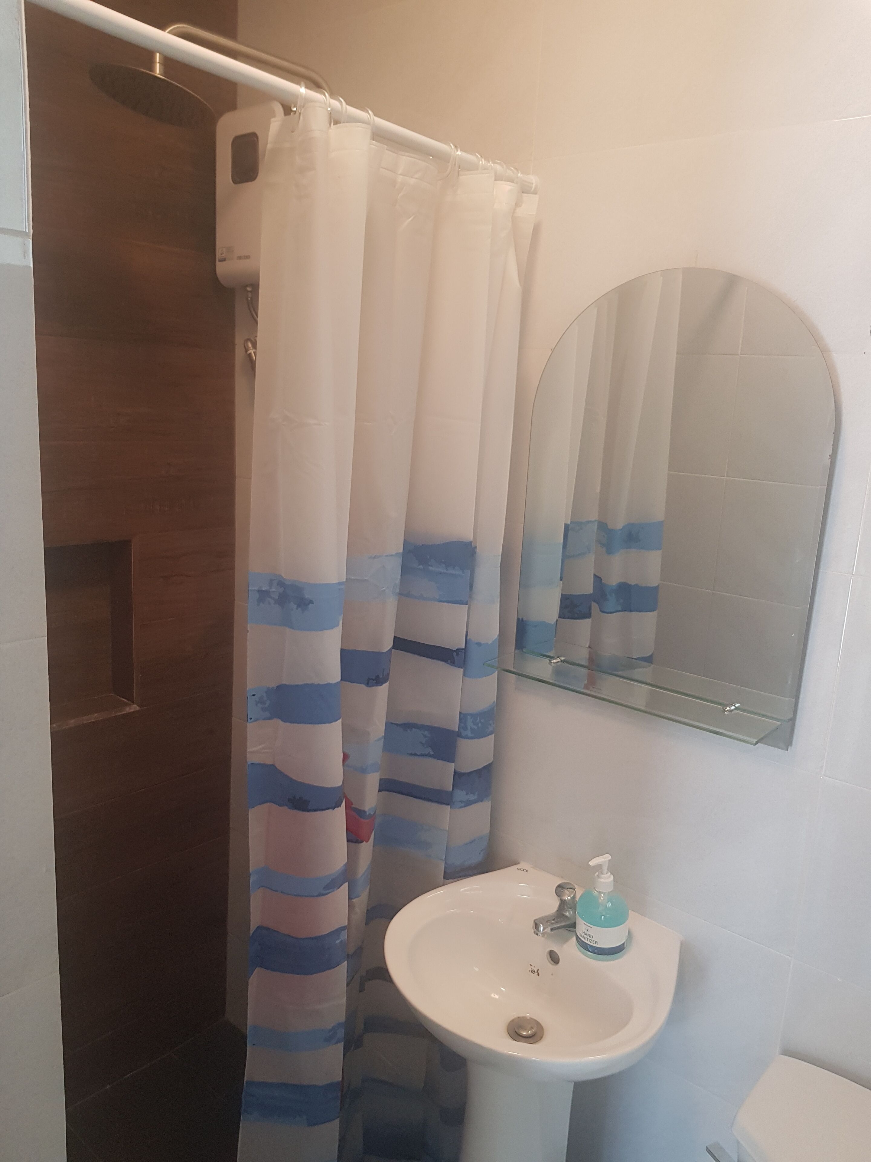 Een badkamer met douchegordijn, wastafel met zeepdispenser en spiegel.