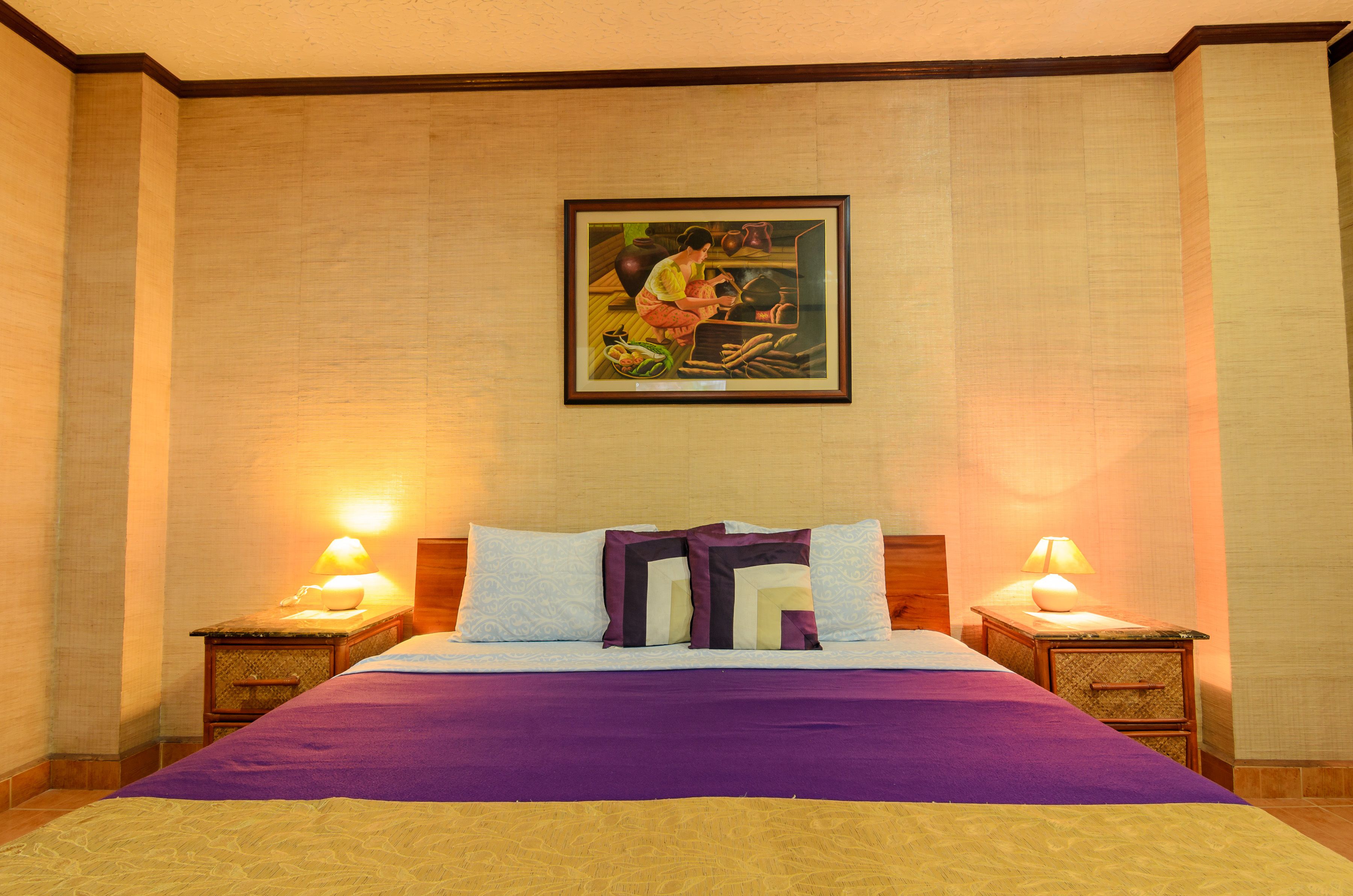 A hotel room with a bed, two bedside tables, a nightstand, a framed picture on the wall, and a lamp on each bedside table.