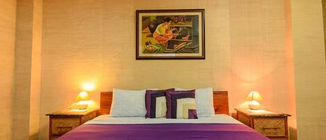 A hotel room with a bed, two bedside tables, a nightstand, a framed picture on the wall, and a lamp on each bedside table.