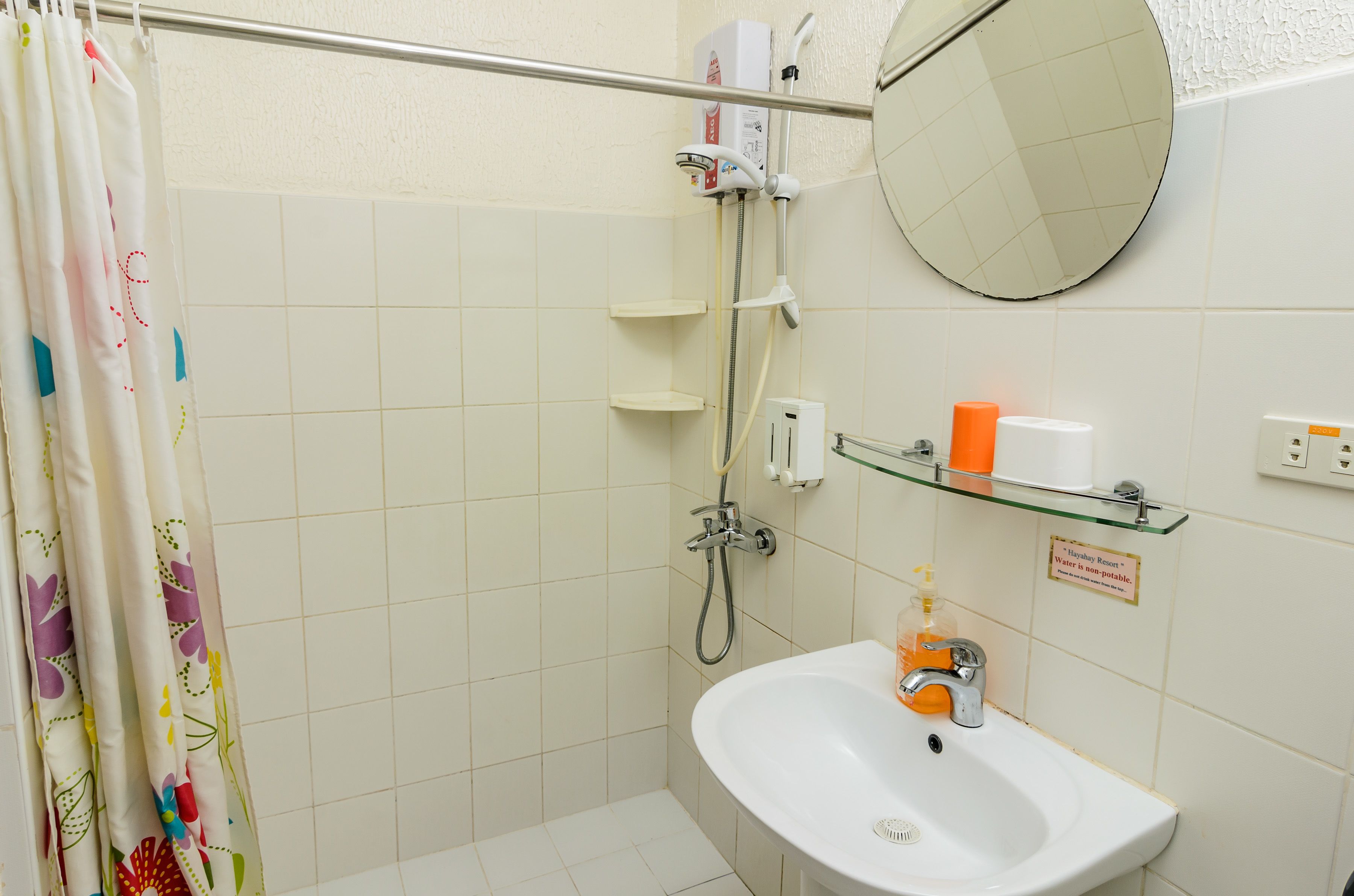 A bathroom with a shower, a sink, a mirror, and a shelf with toiletries.