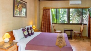 A hotel room with a bed, a ceiling fan, a window with curtains, a chair, and a small table.